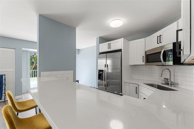 kitchen with light stone countertops, sink, stainless steel appliances, kitchen peninsula, and white cabinets