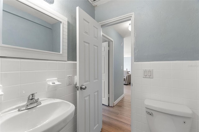 bathroom featuring toilet, wood-type flooring, sink, and tile walls