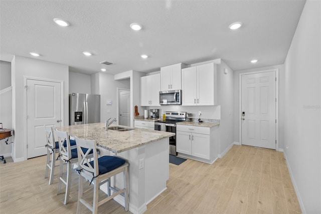 kitchen with a kitchen island with sink, light hardwood / wood-style floors, light stone counters, white cabinetry, and stainless steel appliances