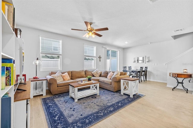 living room featuring ceiling fan, light wood-type flooring, and a textured ceiling