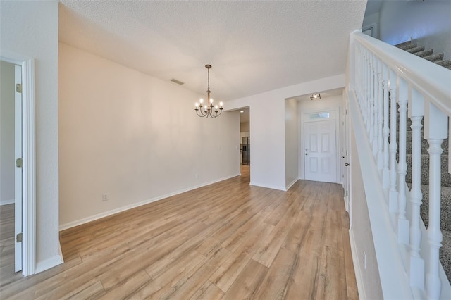 unfurnished room featuring a textured ceiling, an inviting chandelier, and light hardwood / wood-style flooring