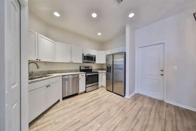 kitchen featuring appliances with stainless steel finishes, light stone counters, sink, light hardwood / wood-style floors, and white cabinetry