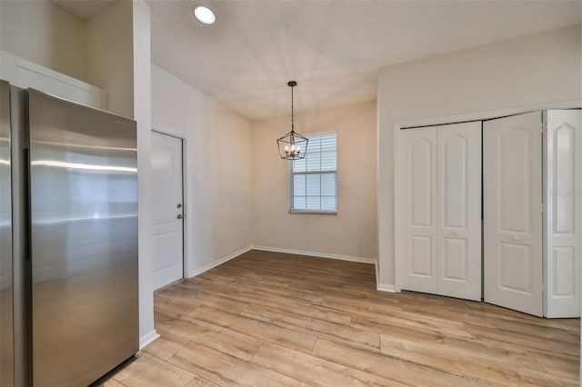 unfurnished dining area featuring a notable chandelier, light hardwood / wood-style floors, and a textured ceiling