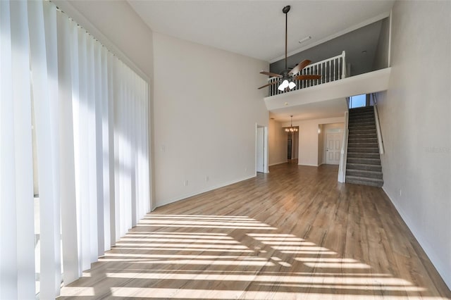 unfurnished living room featuring ceiling fan with notable chandelier, a towering ceiling, and hardwood / wood-style flooring