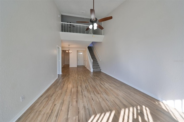 unfurnished living room featuring ceiling fan with notable chandelier, light hardwood / wood-style floors, and a towering ceiling