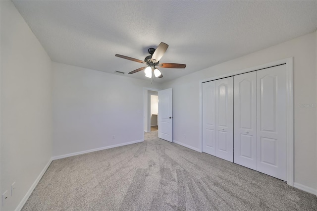 unfurnished bedroom featuring ceiling fan, a closet, light colored carpet, and a textured ceiling