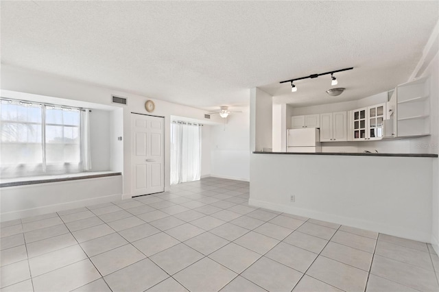 empty room with ceiling fan, light tile patterned flooring, a textured ceiling, and track lighting