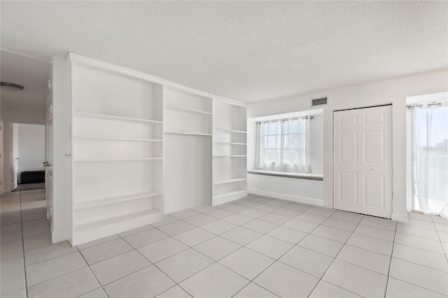 empty room featuring built in shelves, a textured ceiling, and light tile patterned flooring