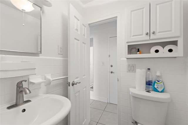 bathroom with toilet, tile patterned floors, tile walls, and sink