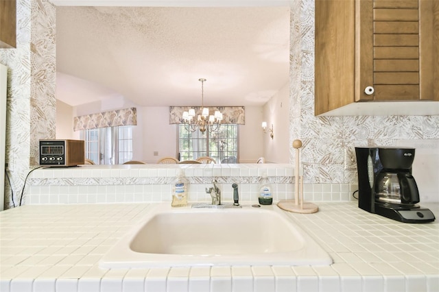 kitchen featuring kitchen peninsula, sink, pendant lighting, and a notable chandelier