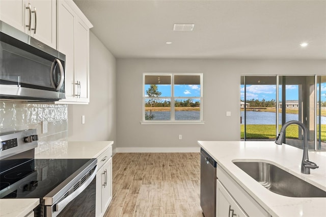 kitchen with sink, white cabinets, light stone counters, stainless steel appliances, and a water view