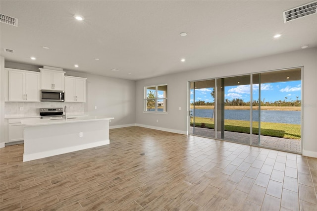 kitchen featuring a water view, white cabinetry, stainless steel appliances, and a center island with sink