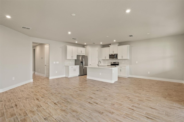 kitchen with white cabinetry, a center island with sink, stainless steel appliances, light hardwood / wood-style floors, and backsplash