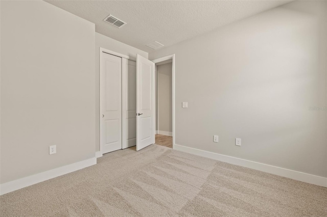 unfurnished bedroom with light carpet, a textured ceiling, and a closet