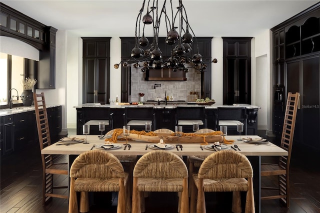 kitchen with an inviting chandelier, dark hardwood / wood-style floors, an island with sink, decorative backsplash, and a breakfast bar