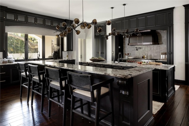 kitchen featuring pendant lighting, dark wood-type flooring, a large island with sink, a kitchen breakfast bar, and light stone counters