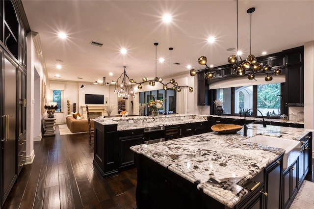 kitchen with dark hardwood / wood-style flooring, light stone counters, a spacious island, sink, and decorative light fixtures