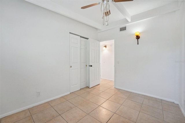 tiled empty room featuring beamed ceiling and ceiling fan