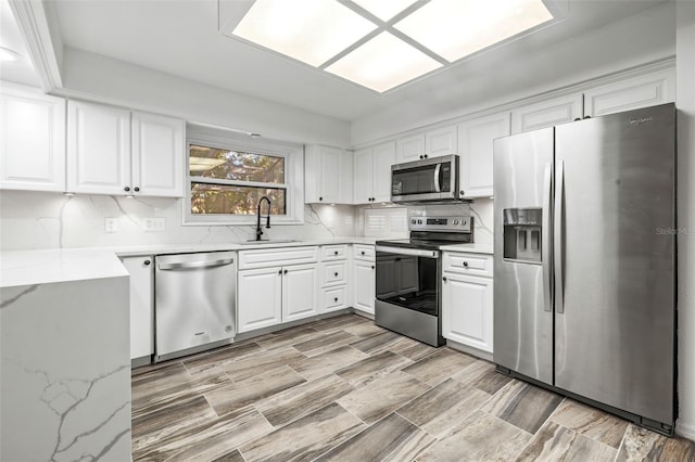 kitchen featuring light stone countertops, appliances with stainless steel finishes, tasteful backsplash, sink, and white cabinetry