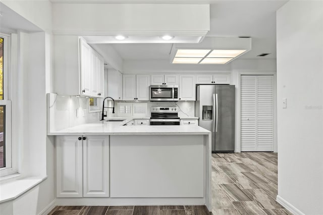 kitchen featuring white cabinetry, sink, stainless steel appliances, light hardwood / wood-style flooring, and kitchen peninsula