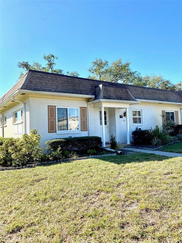 view of front of home featuring a shingled roof, a front yard, brick siding, and mansard roof