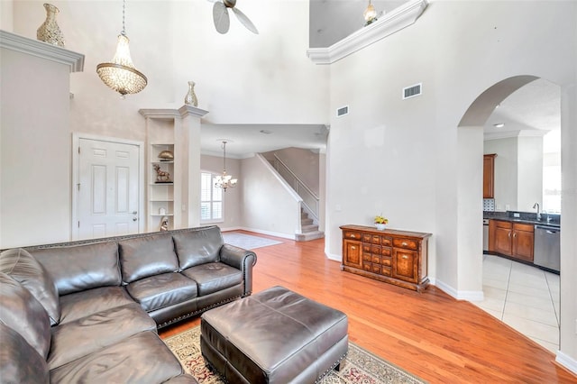 living room featuring ceiling fan with notable chandelier, light wood-type flooring, crown molding, and a high ceiling