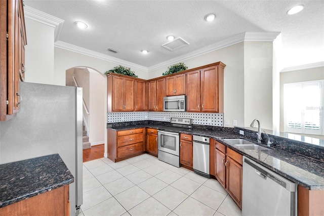 kitchen featuring backsplash, dark stone counters, crown molding, sink, and appliances with stainless steel finishes