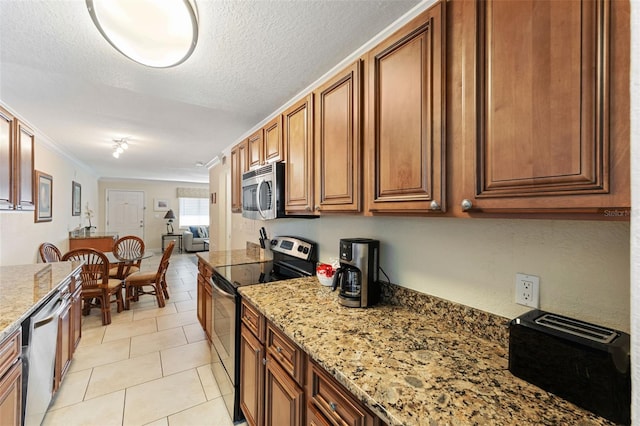 kitchen with light stone countertops, crown molding, a textured ceiling, light tile patterned flooring, and appliances with stainless steel finishes