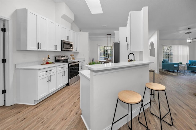 kitchen featuring a kitchen breakfast bar, kitchen peninsula, white cabinets, and stainless steel appliances