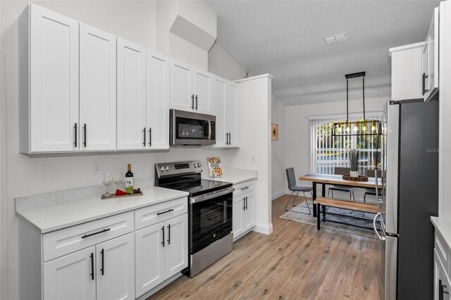 kitchen with light wood-type flooring, a textured ceiling, stainless steel appliances, white cabinets, and hanging light fixtures