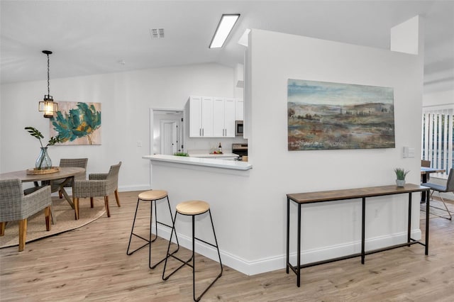 kitchen featuring white cabinetry, light hardwood / wood-style flooring, kitchen peninsula, pendant lighting, and vaulted ceiling