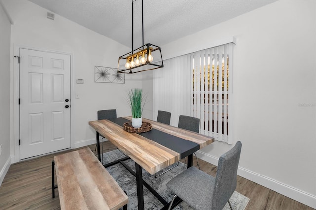 dining room with a textured ceiling, hardwood / wood-style flooring, and lofted ceiling