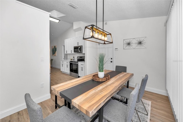 dining space with light hardwood / wood-style floors, lofted ceiling, and a textured ceiling