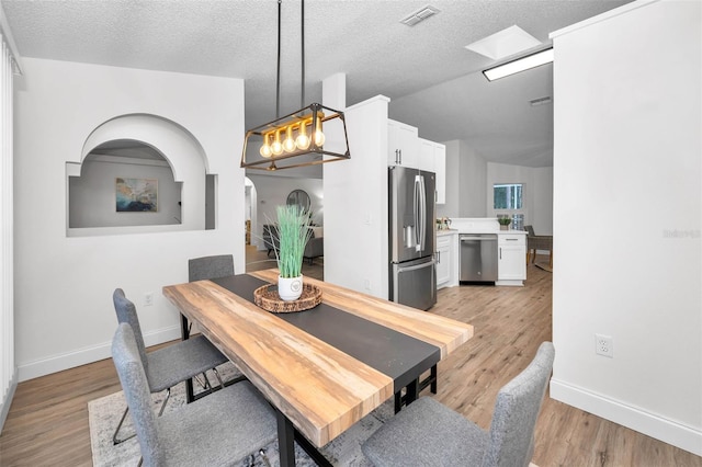 dining area featuring a textured ceiling, an inviting chandelier, light hardwood / wood-style flooring, and lofted ceiling