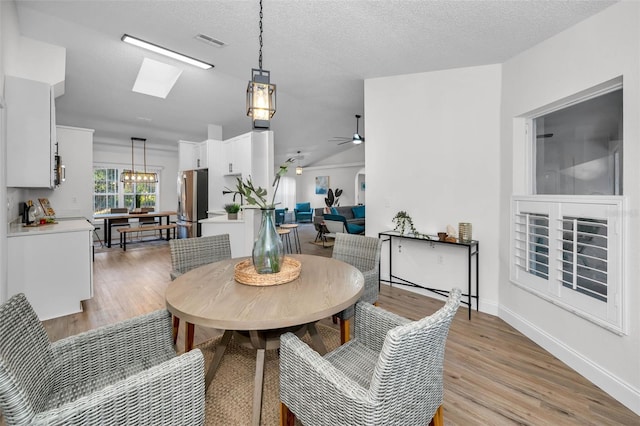 dining area featuring ceiling fan, a skylight, a textured ceiling, and light hardwood / wood-style flooring