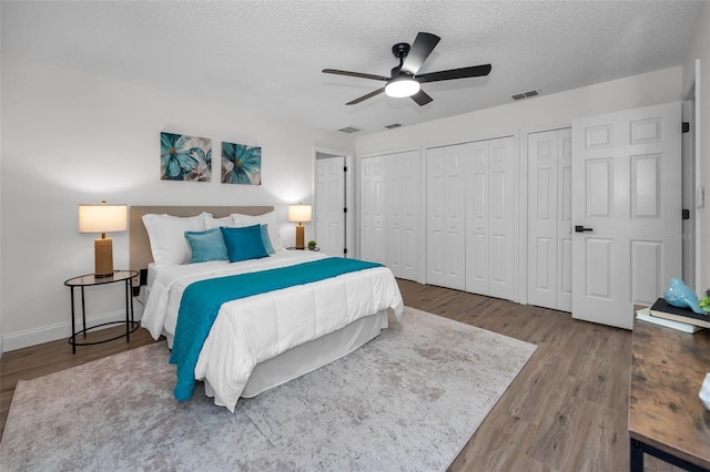 bedroom with ceiling fan, wood-type flooring, a textured ceiling, and multiple closets