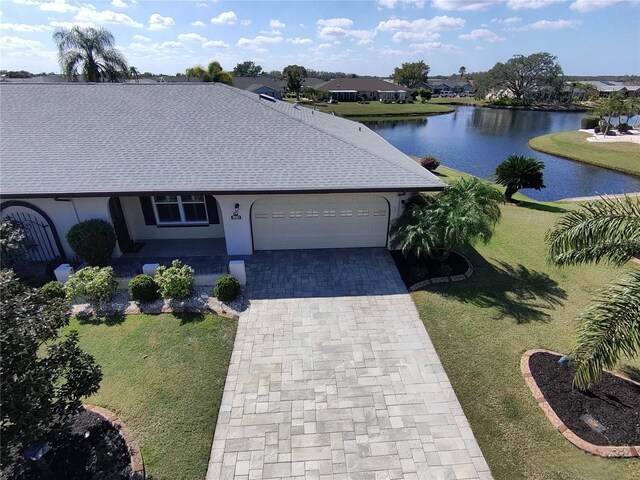 ranch-style home featuring an attached garage, a water view, roof with shingles, decorative driveway, and a front lawn