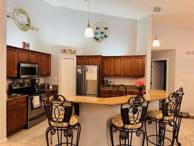 kitchen with a kitchen bar, appliances with stainless steel finishes, a towering ceiling, light tile patterned floors, and hanging light fixtures