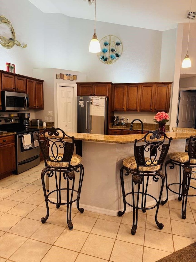 kitchen with light stone countertops, appliances with stainless steel finishes, light tile patterned floors, and a breakfast bar area