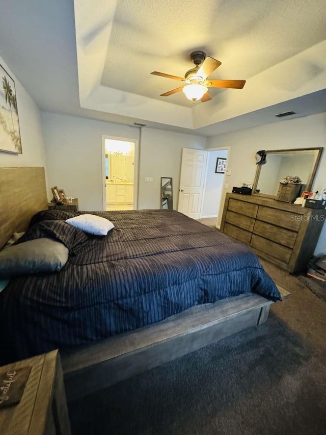 carpeted bedroom featuring ceiling fan, ensuite bath, and a tray ceiling