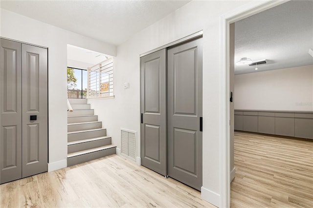 hall with a textured ceiling and light hardwood / wood-style flooring