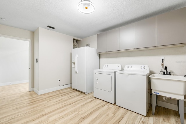 laundry area with cabinets, a textured ceiling, sink, light hardwood / wood-style flooring, and washing machine and clothes dryer