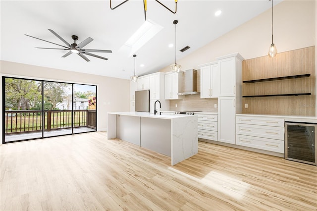 kitchen with pendant lighting, white cabinetry, beverage cooler, and wall chimney exhaust hood