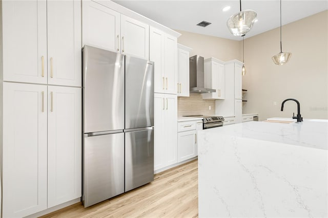 kitchen featuring sink, hanging light fixtures, wall chimney range hood, white cabinets, and appliances with stainless steel finishes