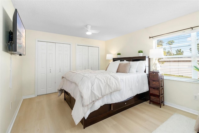 bedroom with ceiling fan, light hardwood / wood-style floors, a textured ceiling, and multiple closets