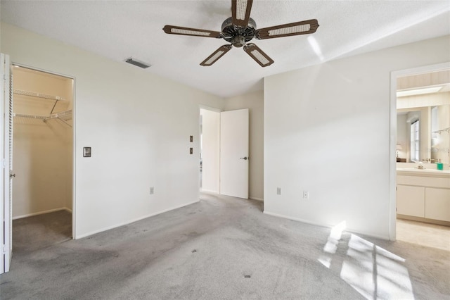 unfurnished bedroom with light carpet, a walk in closet, ceiling fan, connected bathroom, and a closet