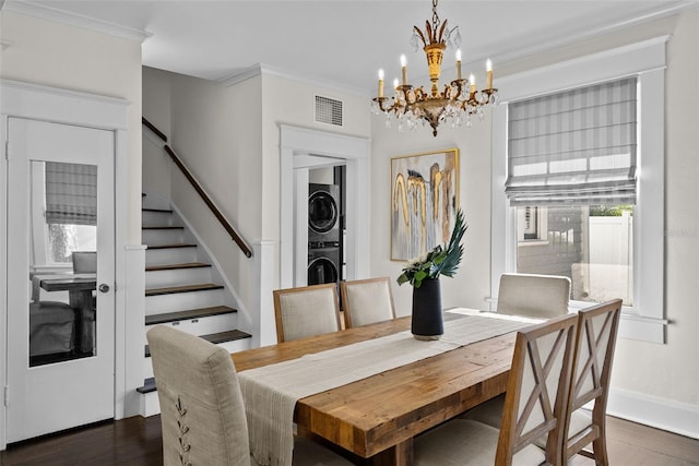 dining space featuring dark hardwood / wood-style flooring, an inviting chandelier, stacked washer / dryer, and ornamental molding