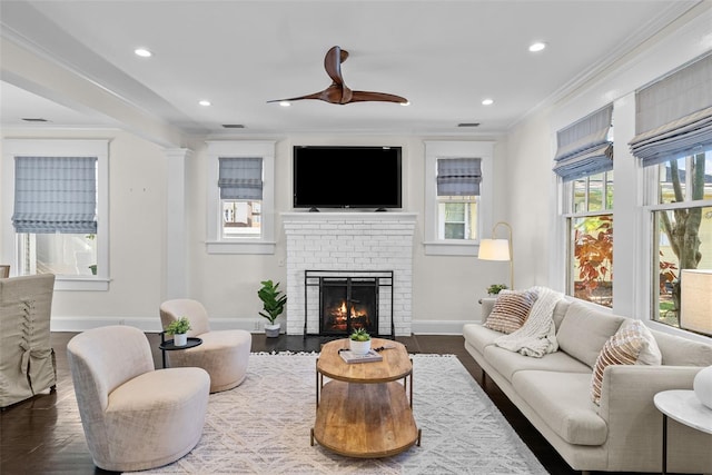 living room with wood-type flooring, a brick fireplace, ceiling fan, and crown molding