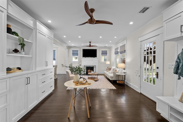 living room featuring ceiling fan, plenty of natural light, dark hardwood / wood-style floors, and a brick fireplace