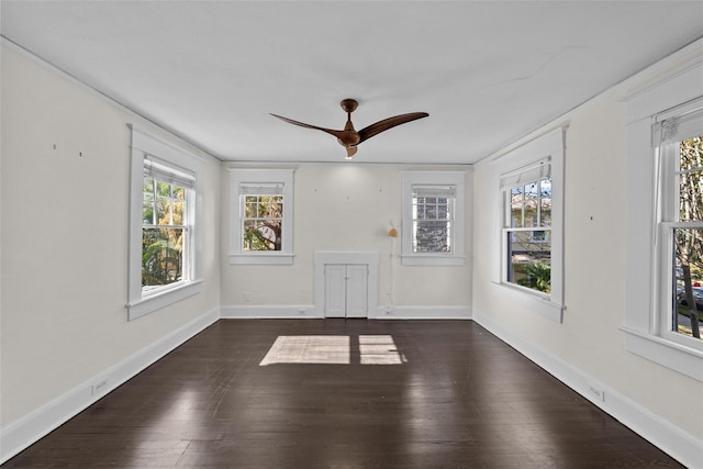 empty room featuring plenty of natural light, ceiling fan, and dark wood-type flooring